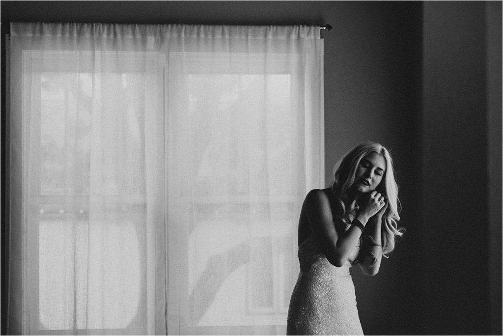 black and white image of bride putting her earrings on