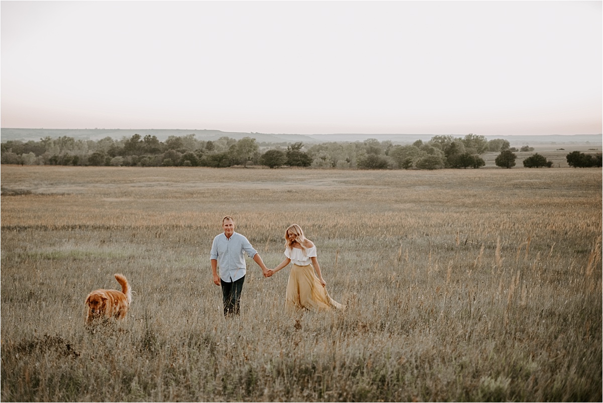 vast photo of couple holding hands in tall grass and dog leading